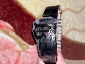 Svart och beige Burberry bälte - Snyggt Burberry bälte med klassiskt rutigt mönster i svart och beige. Bältet har en stilren metallspänne med Burberry-logga i guld. Ena sidan är helsvart med diskret rutstruktur, andra sidan har det ikoniska Burberry-rutiga mönstret. Perfekt accessoar för att lyfta din outfit.