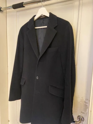 Blå rock från Oscar Jacobson - Exklusiv marinblå rock från Oscar Jacobson med tailored passform. Kavajen har 3 knappar framtill, och två fickor. Perfekt för dig som vill ha en tidlös och elegant look. Materialet är mjukt, en kashmir och ullblend.