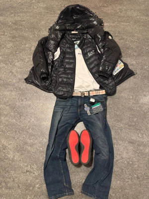 Svart Moncler Maya S - Svart Moncler Maya från Moncler i storlek S. Jackan har glansig finish, huva och klassisk Moncler-logga på ärmen. Fylld med vitt gåsdun för extra värme. Perfekt för dig som vill ha en snygg och lyxig vinterjacka med street vibe.