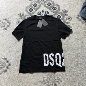Svart DSQUARED2 t-shirt med tryck - Svart t-shirt från DSQUARED2 med stort vitt DSQ2-tryck nere vid fållen. Klassisk passform med rund hals och korta ärmar. Tillverkad i mjuk bomull som känns skön mot huden. Perfekt för dig som gillar stilrena plagg med en twist.