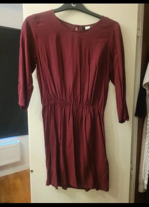 Vinröd klänning  - Snygg vinröd klänning från HM i storlek 36. Modellen har rund hals, resår i midjan och trekvartsärm. Klänningen är kort och har en enkel, stilren design som är lätt att matcha. .