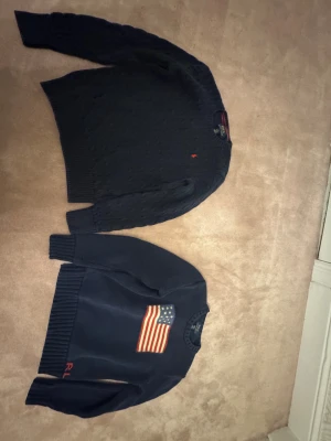 Mörkblå stickad tröja Polo Ralph Lauren - Snygg mörkblå stickad tröja från Polo Ralph Lauren med kabelstickat mönster och liten röd logga på bröstet. Rund hals och långa ärmar med breda ribbade muddar. Perfekt för dig som gillar klassisk stil med en modern touch.( priset är bara för en)