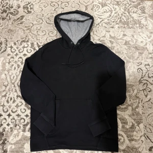 Svart hoodie från BOSS med broderad logga - Svart hoodie från BOSS med broderad logotyp framtill. Tröjan har huva med snörning, ribbade muddar och en stor magficka. Insidan av huvan är ljusgrå vilket ger en snygg kontrast. Perfekt för dig som gillar stilrena och bekväma plagg.