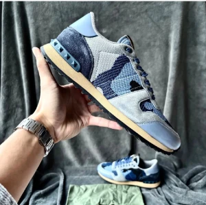 Valentino Rockrunner blå sneakers - Säljer ett par Valentino Rockrunner sneakers i olika blå nyanser med camouflagemönster. Skorna har detaljer i mocka, mesh och skinn, samt ikoniska nitar på hälen. Rund tå, snörning och platt sula. Perfekt för dig som gillar exklusiva och unika sneakers. Självklart äkta ✅, storlek 40 passar 41-41.5