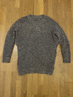Grå stickad tröja från COS - Säljer en snygg brun/rosamelerad stickad tröja från COS i storlek M. Tröjan har rund hals, långärmade ärmar och en loose passform. Materialet är mjukt och värmande, perfekt för kyliga dagar. Enkel och stilren design som funkar till jeans eller cargo.