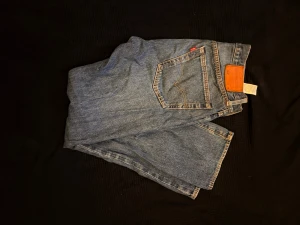 Levi's 501 blå jeans - Klassiska Levi's 501 jeans i ljusblå denim med raka ben . Snyggt läderpatch bak i midjan och den ikoniska röda Levi's-taggen på bakfickan. Perfekta för dig som gillar tidlös stil och vill ha ett par jeans som alltid funkar.