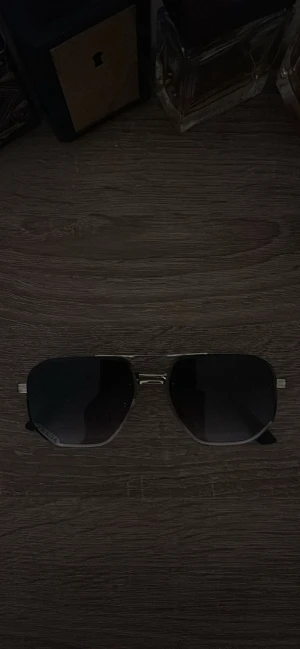 Svarta solglasögon från Prada - Snygga svarta solglasögon från Prada med metallbågar och rektangulära linser i mörktonat glas. Tunn ram i silverfärgad metall och svarta skalmar med Prada-logga på sidan. Perfekt för dig som vill ha en stilren och lyxig look.