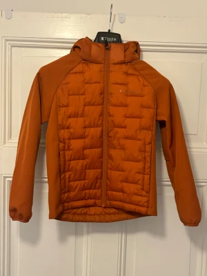 Orange quiltad pufferjacka från Everest - Snygg orange pufferjacka från Everest med huva och hel dragkedja. Storlek 134-140. Sparsamt använt av ett barn under en säsong. Jackan har quiltad framsida och baksida, långärmade släta ärmar och en sportig look. Perfekt för dig som gillar färg och vill sticka ut lite extra. 
