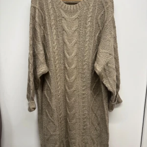 Beige stickad klänning från lager 157 - Säljer en beige stickad klänning från lager 157 i storlek L. Klänningen har ett snyggt flätmönster framtill och på ärmarna, rund hals och långa ärmar. Perfekt för dig som gillar en chill och cozy stil under hösten och vintern. Aldrig använd bara klippt av prislapp! 