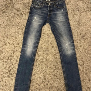 Jeans med slitningar 27/32 - Snygga blå jeans från Jack & Jones, modell Slim Glenn. De har en slim passform, klassisk femficksdesign och slitna detaljer framtill. Jeansen är tillverkade i denim med lätt stretch och har en medelhög midja. Perfekta för en avslappnad och trendig look. 