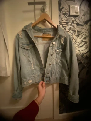 Ljusblå  jeansjacka - Säljer en ljusblå jeansjacka med slitna detaljer och klassiska knappar framtill. Jag har vikt upp ärmarna men det går lätt att vika tillbaka också! 