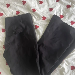 Svarta byxor från Gina Tricot XL - Svarta byxor från Gina Tricot i storlek XL. Bot cut modell med knappstängning och ficka med lock på sidan. Snyggt och enkelt snitt som passar till många olika stilar. Materialet känns mjukt och bekvämt mot huden.