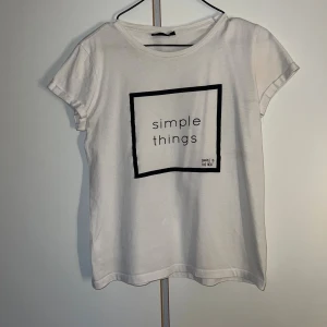 Vit t-shirt med tryck från KappAhl - Vit t-shirt från KappAhl i bomull med svart fyrkantigt tryck och texten 'simple things' på bröstet. Klassisk rund halsringning och korta ärmar. Perfekt för en clean och chill stil.