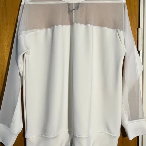 Vit långärmad tröja med meshdetaljer - Säljer en vit långärmad tröja i storlek small med transparenta meshpartier över axlar och ärmar. Tröjan har en clean och modern look med rund halsringning och mjukt material. Avklippt etikett men inget som skadat plagget.  