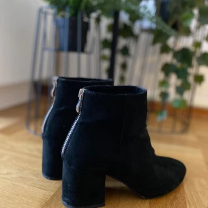 Svarta mocka stövletter med klack - Snygga svarta stövletter i mocka med rund tå och bred klack. Dragkedja baktill för en clean look och enkel påtagning. Perfekta till jeans eller kjol när du vill ha en stilren vibe. Stearinljus och repor 