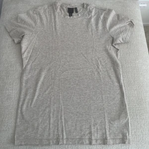 Ljusgrå basic t-shirt från H&M - Enkel och stilren ljusgrå t-shirt från H&M i mjuk bomull. Klassisk rund halsringning och korta ärmar. Perfekt för en clean och avslappnad look.