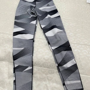 Adidas leggings med svartvitt mönster - Snygga leggings från Adidas med grafiskt svartvitt mönster. De är tighta och har hög midja, perfekta för träning eller chill. Materialet är stretchigt och andas, vilket gör dem riktigt bekväma. Adidas-loggan syns diskret på höften.