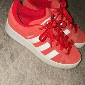 Adidas Campus röda sneakers strl 36 - Säljer ett par Adidas Campus sneakers i rött mocka med vita klassiska stripes och vit sula. Skorna har röda snören och en låg profil, perfekt för dig som gillar streetstyle. Adidas-logga på plösen och sidan. Snygga och tidlösa sneakers för alla tillfällen.