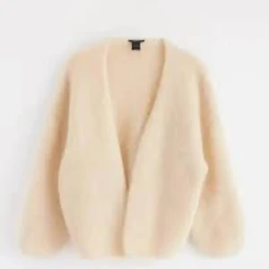 Beige fluffig kofta med v-ringning - Supermjuk och fluffig beige kofta med v-ringad öppning och långa ärmar. Perfekt för att slänga över en t-shirt eller linne när du vill ha en chill och cozy vibe. Materialet känns lyxigt och har en lätt oversized passform.