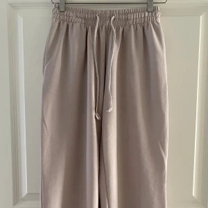 Beige mjukisbyxor från 157 - Säljer ett par beige mjukisbyxor från 157 med bred resår i midjan och snörning. Byxorna har en loose passform och raka ben, perfekta för chill dagar. Tillverkade i mjukt material som känns skönt mot huden.