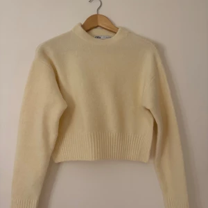 Ljusbeige stickad tröja från Zara - Supermysig ljusbeige stickad tröja från Zara med croppad passform och ribbade muddar vid ärmslut och nederkant. Tröjan har en enkel design med rund hals och långa ärmar, perfekt för att hålla dig varm under kyliga dagar.