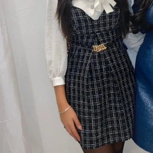 Rutig svartvit tweed klänning från Reserved - Supersnygg kort tweed klänning från Reserved i svartvitt rutigt tyg. Klänningen har breda axelband, markerad midja med guldfärgad kedjedetalj och dragkedja bak. Perfekt för dig som gillar en chic och trendig look. M enligt etiketten men är mer som S. 