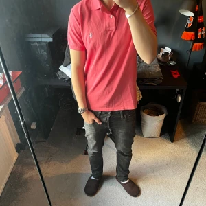 Ralph Lauren pikétröja  - Säljer en klassisk rosa pikétröja från Ralph Lauren med vit broderad logga på bröstet. Tröjan har korta ärmar, krage och knappar vid halsen. Perfekt för dig som vill ha en stilren och fräsch look. Skriv för fler bilder