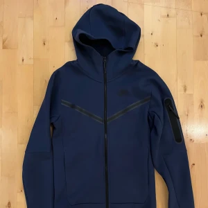 Nike Tech Fleece Mörkblå XS - Riktigt fet Nike Tech i mörkblå färg. Aldrig använd, så den är i  toppskick. Storlek XS, sitter snyggt och stilrent. Perfekt för dig som vill en fet hoodie som passar både vintern och sommarn