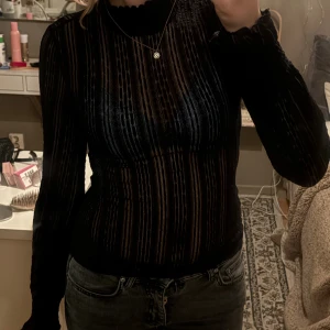 Svart transparent spets topp från Noisy May - Säljer en svart transparent långärmad topp från Noisy May. Toppen har ett randigt mönster i tyget och hög hals med volangkant. Den är figurnära och perfekt att styla lager på lager. Materialet känns lätt och stretchigt. Spetstopp