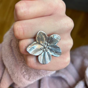 Stor blom ring i rostfritt stål - Säljer en statementring i silverfärg med en stor, detaljerad blomma som motiv. Ringen har tydliga ådringar på blombladen och en justerbar ringbas. Perfekt för dig som vill sticka ut med en unik accessoar.