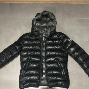 Svart dunjacka från Colmar med huva - Snygg svart vinterjacka från Colmar. Jackan har huva, dragkedja framtill och två fickor med dragkedja. Jackan är i mycket fint skick. Skriv för fler bilder.