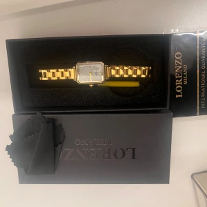 Guldfärgad klocka Lorenzo Milano - Snygg guldfärgad klocka från Lorenzo Milano med fyrkantig urtavla i silver och klassisk länkarmband. Klockan har romerska siffror och stilren design som ger en lyxig vibe. Perfekt accessoar för att lyfta din outfit.