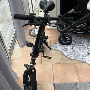 Elcyckel - Smidig och kompakt hopfällbar elcykel i svart med moderna detaljer. Utrustad med skivbromsar, batteri integrerat i ramen och tydliga reglage på styret. Cykeln ser ut att vara i mycket gott skick utan synligt slitage eller defekter. Perfekt för stadspendling och enkel förvaring.