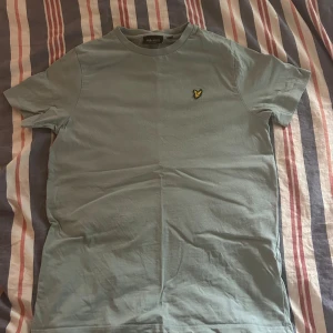 Ljusgrön t-shirt från Lyle & Scott - Snygg ljusgrön t-shirt från Lyle & Scott med klassisk gul logga på bröstet. T-shirten är i mjuk bomull och har en enkel, stilren design med rund hals och korta ärmar. Perfekt för en chill och avslappnad look.