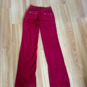 Juciy byxor - Snygga röda mjukisbyxor från juciy med bred resår i midjan och snörning framtill. Byxorna har stora fickor både fram och bak, med lock och knappar bak. Materialet är mjukt och skönt.  Passformen är rak och lite loose. Storlek xxs men passar även mig i xs/s