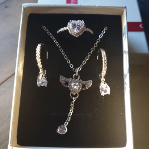 Smyckeset  - Ett glittrande smyckeset i silverfärg med ett justerbart halsband, en ring i strl10,5 (64) och vattendroppar örhängen. Material : koppar och zirkonia. Perfekt för dig som gillar bling och romantiska detaljer.