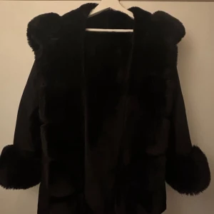 Svart pälsjacka med fluffig huva och händer  - Säljer en svart pälsjacka med fluffig huva och breda pälsdetaljer vid ärmslut och framkant. Jackan har dragkedja och stora fickor framtill. Materialet är päls och syntet, perfekt för kalla dagar när du vill ha en extra mysig vibe. Den är XL från Garoff men jag är M och den passar mig jättebra 