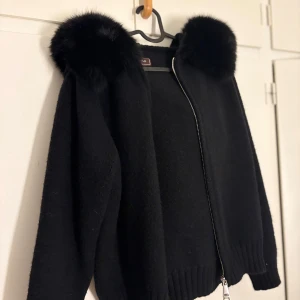 Svart pälsjacka från Alessa - Snygg svart pälsjacka från Alessa med fluffig krage i fuskpäls och ribbade muddar. Jackan har dragkedja framtill och är långärmad. Perfekt för dig som vill ha en stilren och mysig look under kyliga dagar. Använd en gång förra hösten. 