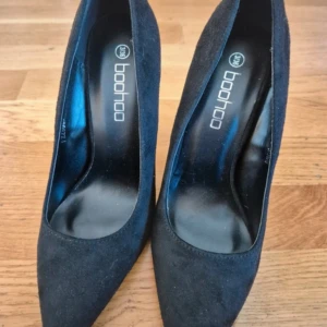 Svarta klackar från Boohoo med klack - Snygga svarta pumps från Boohoo med spetsig tå och hög klack. Skorna är i mockaimitation och har en klassisk, elegant form som passar till många olika outfits. Perfekta för dig som gillar stilrena och trendiga skor.