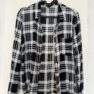 Svartvit rutig skjorta från Amisu - Snygg svartvit rutig skjorta från Amisu i tunn bomull. Skjortan har klassisk krage, lång ärm med manschett och vita knappar framtill. En bröstficka på vänster sida. Perfekt för dig som gillar chill och stilren look.