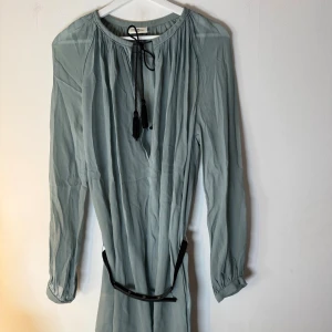 Day Birger et Mikkelsen klänning/lång blus  - Ljusblå klänning/lång blus med långa ärmar och ett svart läderbälte med guldfärgade detaljer. Klänningen har en knytdetalj med tofsar vid halsen. Storlek L. Lite genomskinlig. 