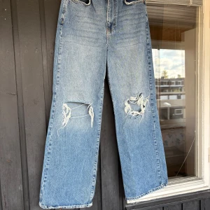 Blå wide jeans med slitna knän - Säljer ett par blåa jeans med breda ben och stora slitningar över båda knäna. 