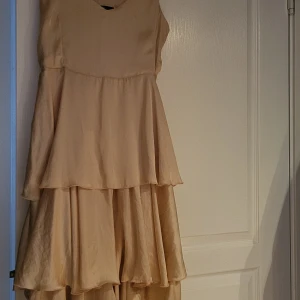 Volangklänning Gina Tricott - Supersöt långklänning från Gina Tricot. Klänningen har flera lager volanger och är ärmlös med rund halsringning. Perfekt för dig som vill ha en flowy och elegant look. Materialet känns lätt och har fin lyster.