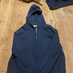 Mörkblå hoodie från Grunt med dragkedja - Säljer en mörkblå hoodie från Grunt i storlek M. Tröjan har huva, lång ärm och en dragkedja framtill. Tillverkad i mjuk bomull och passar perfekt för chill dagar. Enkel och stilren design utan tryck eller mönster. Pris kan diskuteras
