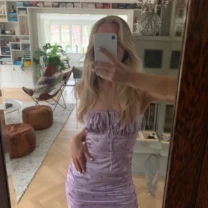 Adoore klänning ”santorini” i storlek 34.  - Supersöt ljuslila kort klänning med små blommor, smockad över bysten och snörning framtill. Klänningen är figurnära och har tunna axelband, perfekt för sommarens varma dagar. Materialet känns lätt och svalt. Köptes för 1399 kr, säljer för endast 499 kr. 