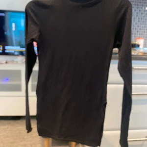 Svart ribbad polotröja Boohoo XS - Svart ribbad polotröja från Boohoo i storlek XS. Tröjan har lång ärm och en tight passform med klassisk polokrage. Perfekt att styla med jeans eller kjol för en clean look. Materialet är mjukt och stretchigt för extra komfort.