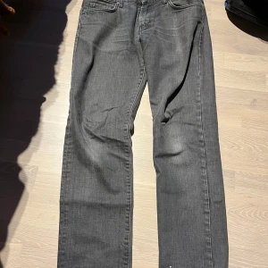 Grå jeans från J.Lindeberg - Snygga grå jeans från J.Lindeberg med klassisk femficksdesign och raka ben. Jeansen har en mörkgrå tvätt. Lite slitna i slutet av benen men det är ingenting man tänker på. Perfekta för dig som gillar stilrena och tidlösa plagg. Storlek 30/32. Tveka inte att skriva vid minsta fundering och priset är absolut inte fast!