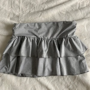 Grå volangkjol i bomull - Supersöt grå kortkjol med dubbla volanger och bred resår i midjan. Kjolen är gjord i mjuk bomull och har en enkel, stilren look som är lätt att matcha. Perfekt för dig som gillar en chill och trendig vibe.