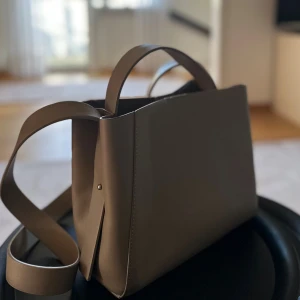 Ljusbrun väska - Säljer denna snygga väska från Ginatricot. Använd fåtal gånger och är i mycket gott skick. Har en ljusbrun/beige snygg färg perfekt nu i höst