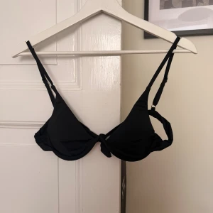 Svart bikiniöverdel med knyt - En stilren svart bikiniöverdel med triangelformade kupor och smala, justerbara axelband som jag köpte utomlands för ett tag sedan. Knytning både fram och bak för en personlig passform. Själva bygeln är som ett ”M”. Kan fota bygeln på begäran. Perfekt för strandhäng eller poolparty. Skulle säga att detta är storlek S. 